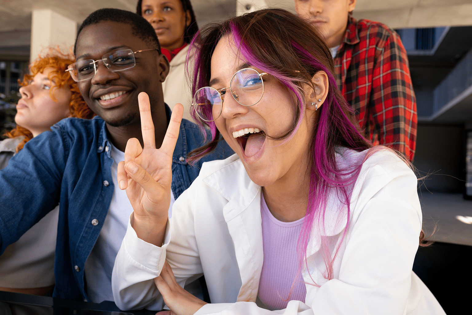 Young woman with purple hair and glasses making a peace sign and smiling.