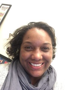 Smiling woman with curly hair and cozy scarf.